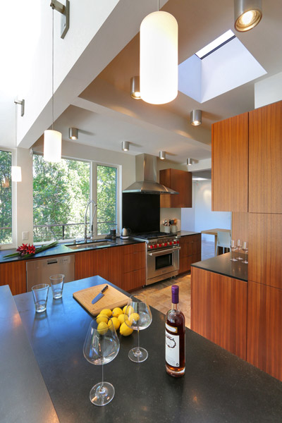 modern kitchen with pendant and canned ceiling lights, wood cabinets, black composite countertops and skylight